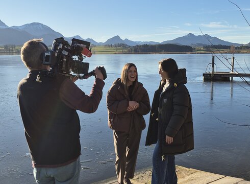 Das Bild zeigt einen Kameramann und zwei Frauen, die vor dem Panorama des Hopfensees ein Interview führen.