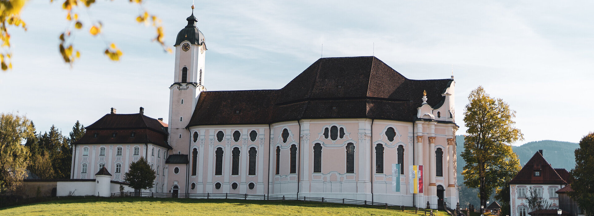 Eine historisch weiße Kirche mit roten Dächern in einer grünen Landschaft.