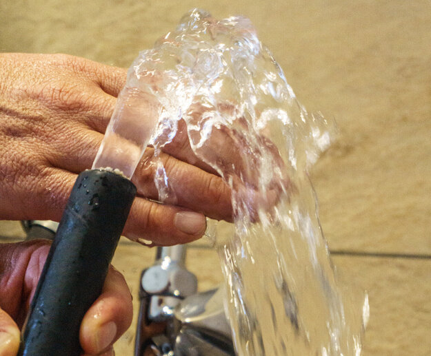 Das Bild zeigt zwei Hände die einen Wasserschlauch halten. Aus dem Wasserschlauch kommt ein klares Wasser, das über die eine Hand läuft. 
