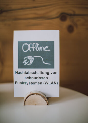 Das Bild zeigt einen Blatt Papier, das in einer Holzhalterung steht. Auf dem Papier ist zu lesen „Nachtabschaltung von schnurlosen Funksystemen (WLAN).
