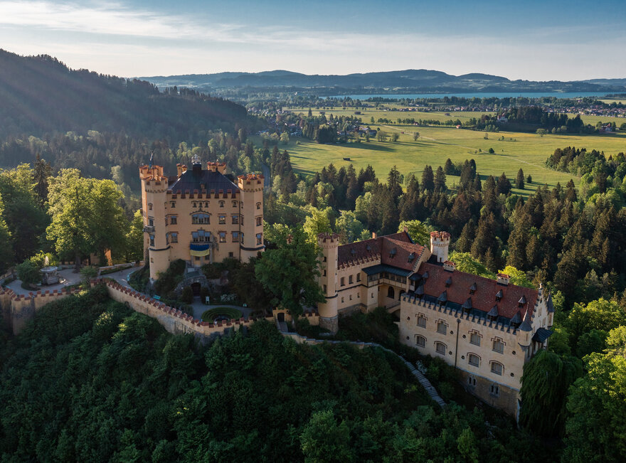 Das prächtige Schloss Hohenschwangau thront auf einem Hügel inmitten einer grünen Landschaft. Die Aussicht bietet eine idyllische Kulisse.
