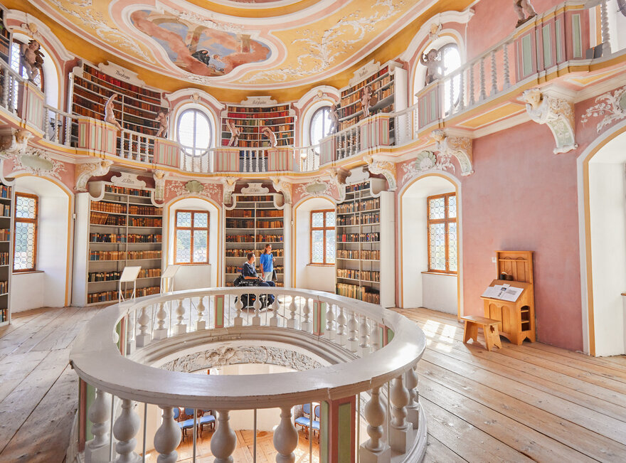 Die Bibliothek des Hohen Schlosses in Füssen mit hohen Regalen und einem beeindruckenden Rundbogen. Das Bild zeigt einen Raum voller Wissen und Geschichte.