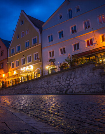Das Bild zeigt ein Gebäude in der Füssener Altstadt mit vielen beleuchteten Fenstern. Der Boden spiegelt das Licht wider.