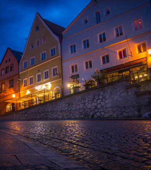 Das Bild zeigt ein Gebäude in der Füssener Altstadt mit vielen beleuchteten Fenstern. Der Boden spiegelt das Licht wider.