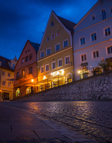 Das Bild zeigt ein Gebäude in der Füssener Altstadt mit vielen beleuchteten Fenstern. Der Boden spiegelt das Licht wider.