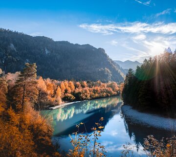Das Bild zeigt den Lech in Füssen umgeben von Wald mit herbstlich rot gefärbtem Laub.