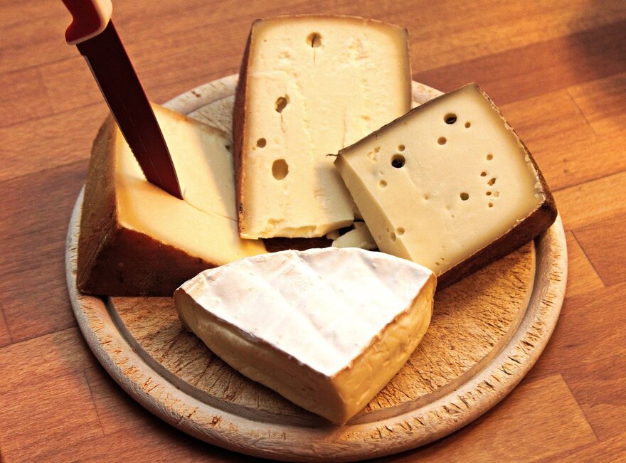  Die Abbildung zeigt ein hölzernes Schneidebrett mit verschiedenen Arten von Käse auf ihm. Der Käse ist geschnitten und auf dem Brett arrangiert.