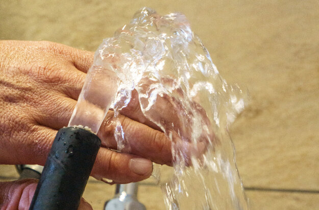 Das Bild zeigt zwei Hände die einen Wasserschlauch halten. Aus dem Wasserschlauch kommt ein klares Wasser, das über die eine Hand läuft. 