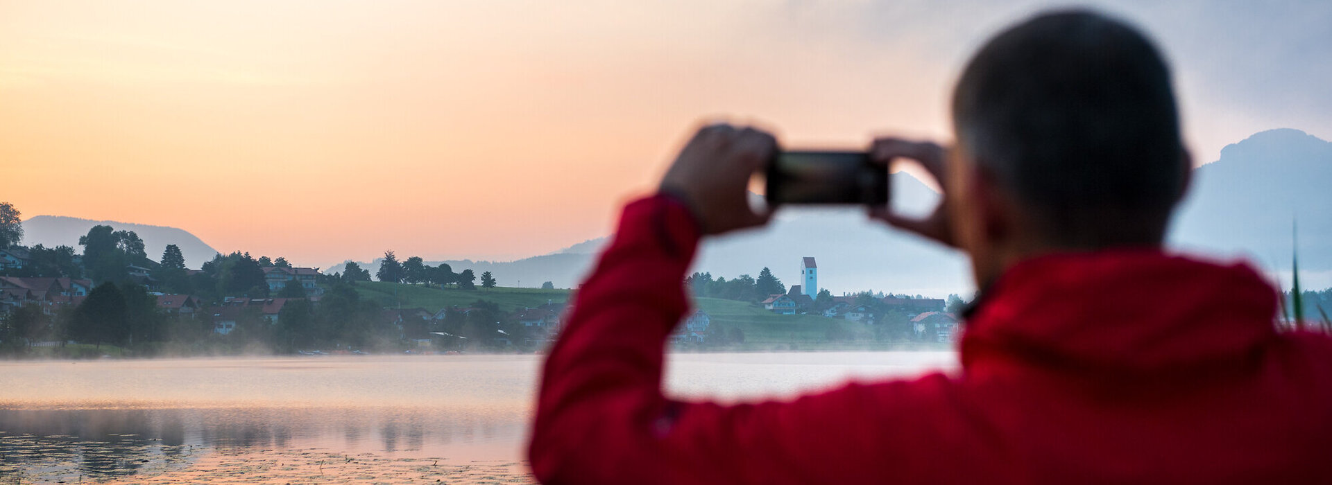 Man takes a photo of a lake at sunset with his smartphone