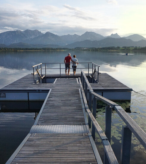 Das Bild zeigt einen großen Steg, der in den Hopfensee ragt. Am Ende des Stegs wird öffnet sich eine Plattform, in deren Mitte ein Kneipptretbecken eingelassen ist. 