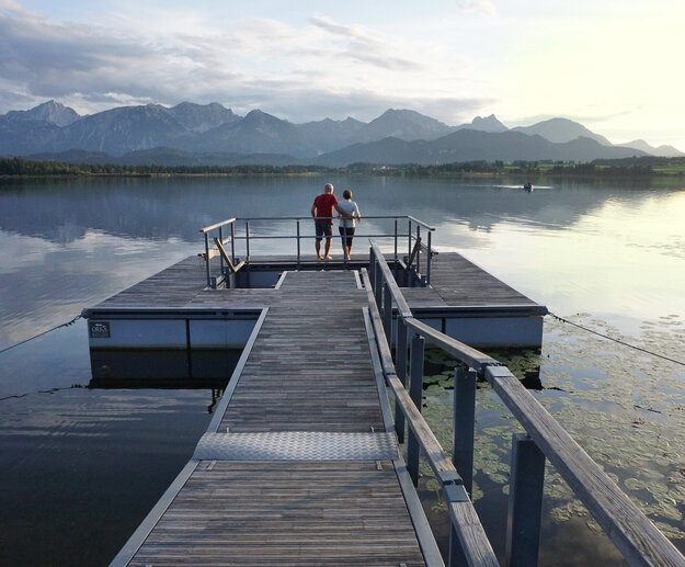 Das Bild zeigt einen großen Steg, der in den Hopfensee ragt. Am Ende des Stegs wird öffnet sich eine Plattform, in deren Mitte ein Kneipptretbecken eingelassen ist. 