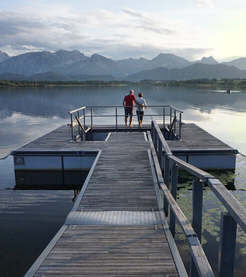 Das Bild zeigt einen großen Steg, der in den Hopfensee ragt. Am Ende des Stegs wird öffnet sich eine Plattform, in deren Mitte ein Kneipptretbecken eingelassen ist. 
