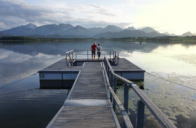 Das Bild zeigt einen großen Steg, der in den Hopfensee ragt. Am Ende des Stegs wird öffnet sich eine Plattform, in deren Mitte ein Kneipptretbecken eingelassen ist. 