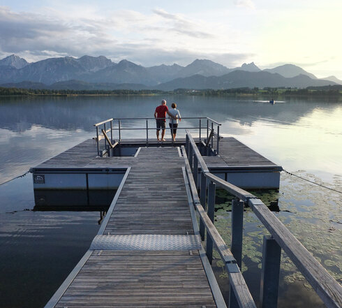 Das Bild zeigt einen großen Steg, der in den Hopfensee ragt. Am Ende des Stegs wird öffnet sich eine Plattform, in deren Mitte ein Kneipptretbecken eingelassen ist. 