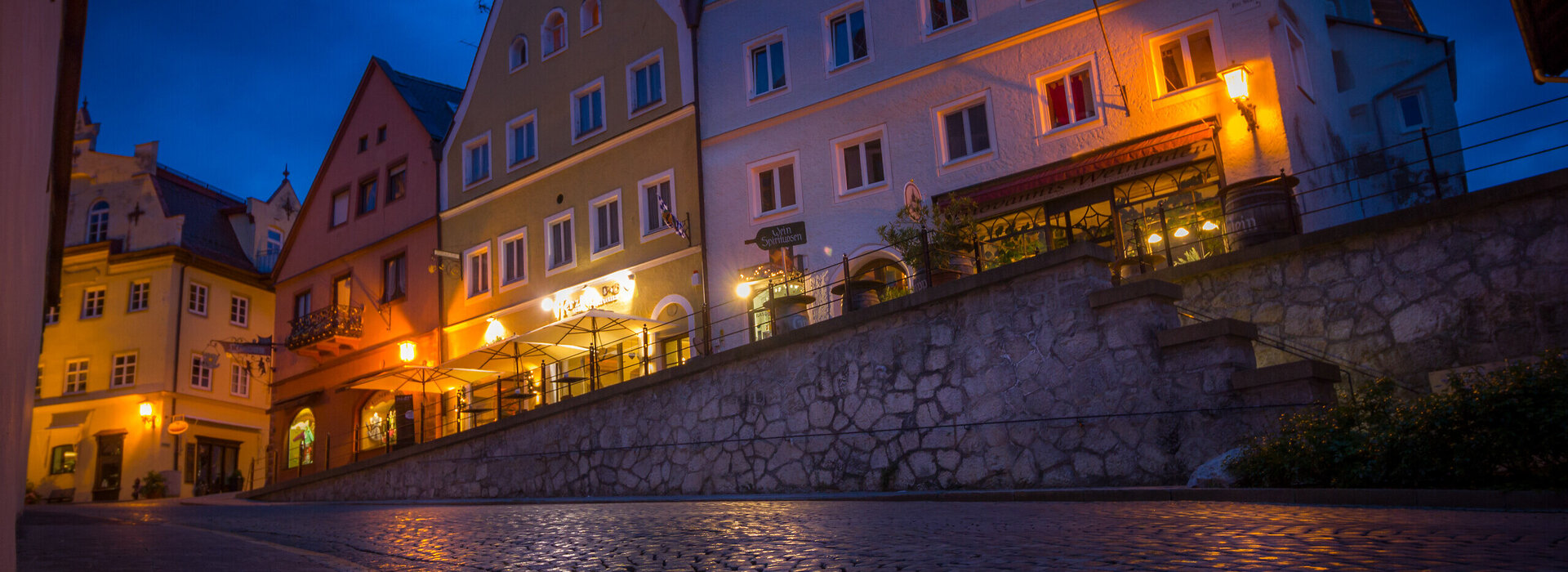 Das Bild zeigt ein Gebäude in der Füssener Altstadt mit vielen beleuchteten Fenstern. Der Boden spiegelt das Licht wider.