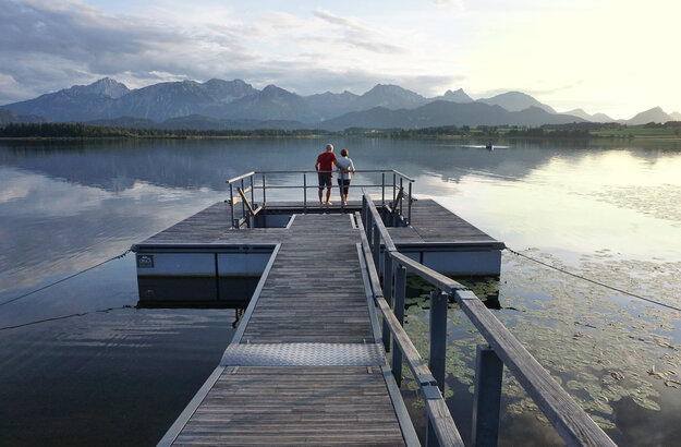 Das Bild zeigt einen großen Steg, der in den Hopfensee ragt. Am Ende des Stegs wird öffnet sich eine Plattform, in deren Mitte ein Kneipptretbecken eingelassen ist. 