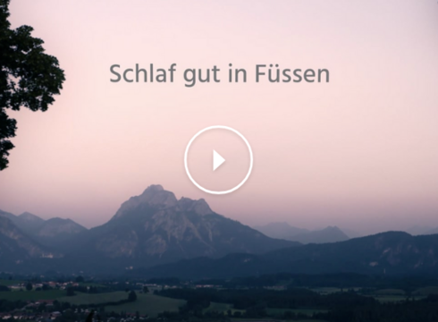 Das Bild zeigt eine in Abendlicht getauchte Landschaft mit einer imposanten Bergkulisse im Hintergrund. Der Himmel leuchtet in Lila- und Blautönen des letzten Sonnenlichts.